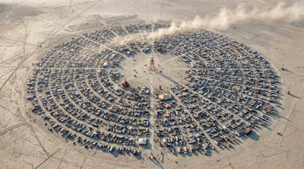 Aerial view of Black Rock City's circular street grid rising from the flat Nevada desert at Burning Man 2026, with the central Man structure visible at the center